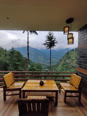 Une table et des chaises en bois sur un balcon avec vue sur la montagne.