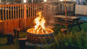 A fire pit with flames, surrounded by wooden benches and a wooden fence with string lights. - Evergreen Pet-friendly Pension, Taean (Taean)