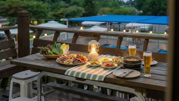 A wooden picnic table with various dishes, a lantern, and a glass of beer.