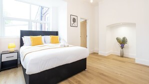 Ein modernes Schlafzimmer mit einem großen Bett, einem Nachttisch, einem Fenster und einer Vase mit Blumen.