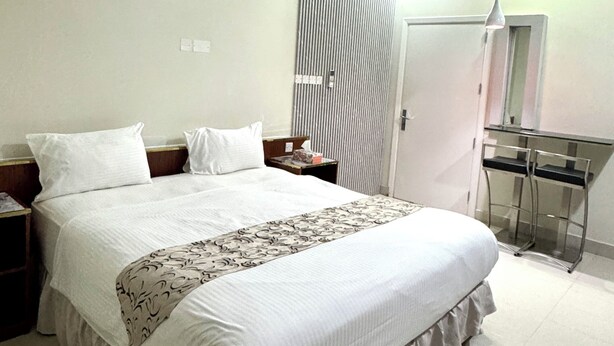 A modern bedroom with a large bed, a bedside table, a desk, and a mirror. - Al Bayrahaa Checkmyguest Muscat  (Seeb)