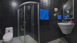 A modern bathroom with a glass-enclosed shower, a white sink, and a black tiled wall. - Al Bayrahaa Checkmyguest Muscat  (Seeb)