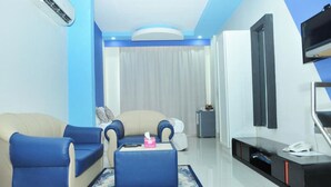 A modern living room with a beige sofa, blue armchairs, a coffee table, a TV, and a phone on a console table. - Al Bayrahaa Checkmyguest Muscat  (Seeb)