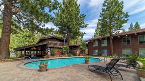 A pool area with lounge chairs and a wooden building with a balcony.