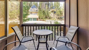A covered outdoor seating area with a table and four chairs, overlooking a residential area with houses and trees.