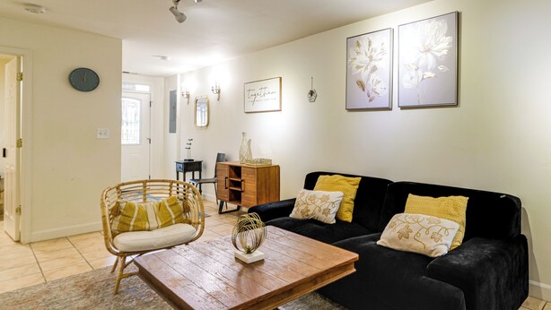 A living room with a black sofa, a wooden coffee table, a wicker chair, and a small wooden cabinet. - 1/2 Mi to Metrobus Stop! Walkable Petworth Duplex (Washington)
