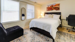 A bedroom with a bed, a black chair, a patterned rug, and a painting on the wall. - 1/2 Mi to Metrobus Stop! Walkable Petworth Duplex (Washington)