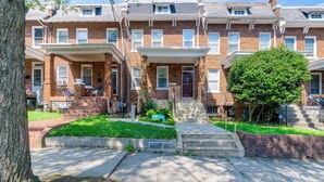 A row of brick townhouses with front porches, a tree in the front yard, and a clear sky. - 1/2 Mi to Metrobus Stop! Walkable Petworth Duplex (Washington)
