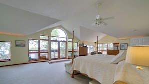 A spacious bedroom with a large bed, a ceiling fan, and a view through a large window. - Lakefront Lookout! Private Sand Beach on Superior (Marquette)