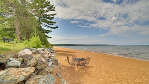 A beach with a table and chairs, surrounded by rocks and trees. - Lakefront Lookout! Private Sand Beach on Superior (Marquette)