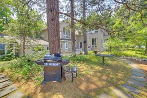A backyard with a grill, a table, and a house in the background. - Private Sandy Beach: Lake Superior Group Retreat (Marquette)