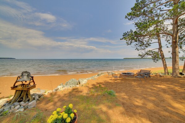 A beach with a wooden bench, a chair, and a small table with a bell. - Private Sandy Beach: Lake Superior Group Retreat (Marquette)