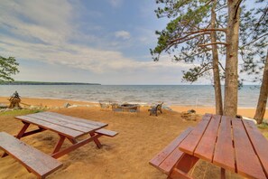 A beach with picnic tables and chairs, a fire pit, and a view of the ocean. - Private Sandy Beach: Lake Superior Group Retreat (Marquette)