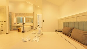 A hotel room with a large bed, a bedside table, a nightstand, a mirror, a bathroom with a sink and a toilet, and a towel rack. - NicestInPhuket4Br1.5kmBangTao BeachV141 (Choeng Thale)