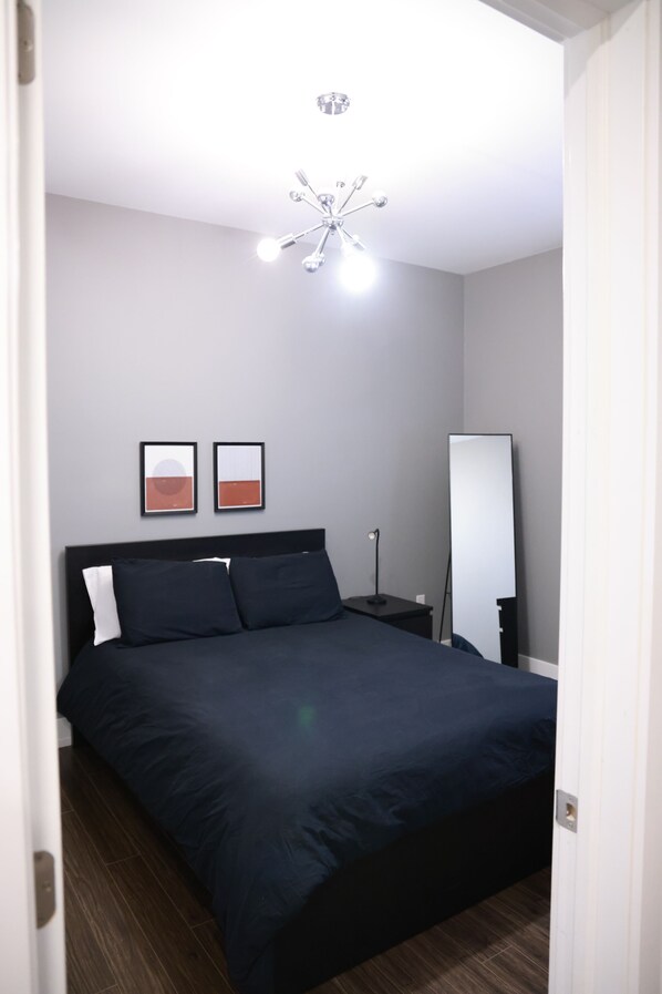 A bedroom with a bed, a bedside table, a lamp, a mirror, and two framed pictures on the wall.