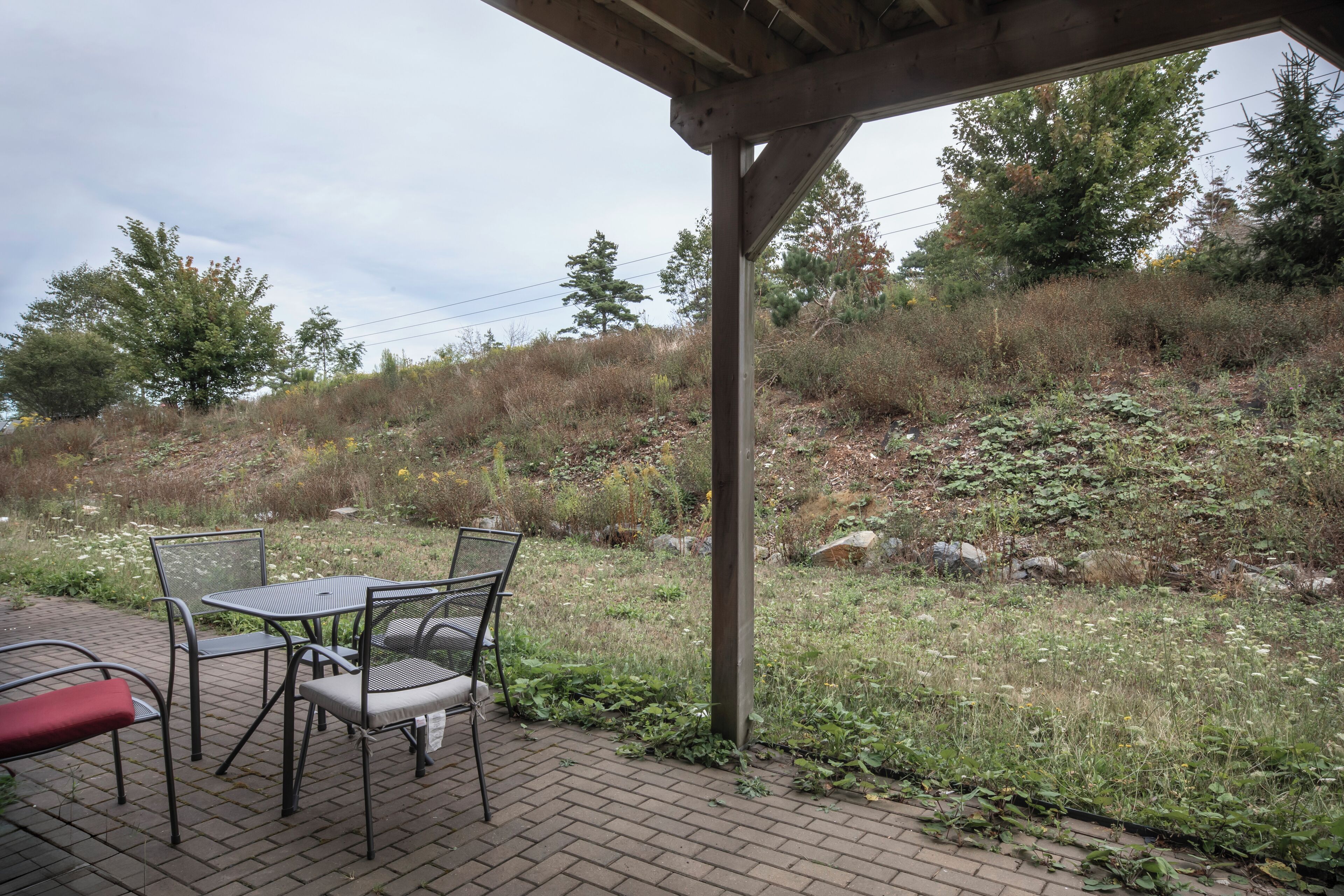 An outdoor patio with a metal table and chairs, surrounded by a natural landscape with trees and shrubs.