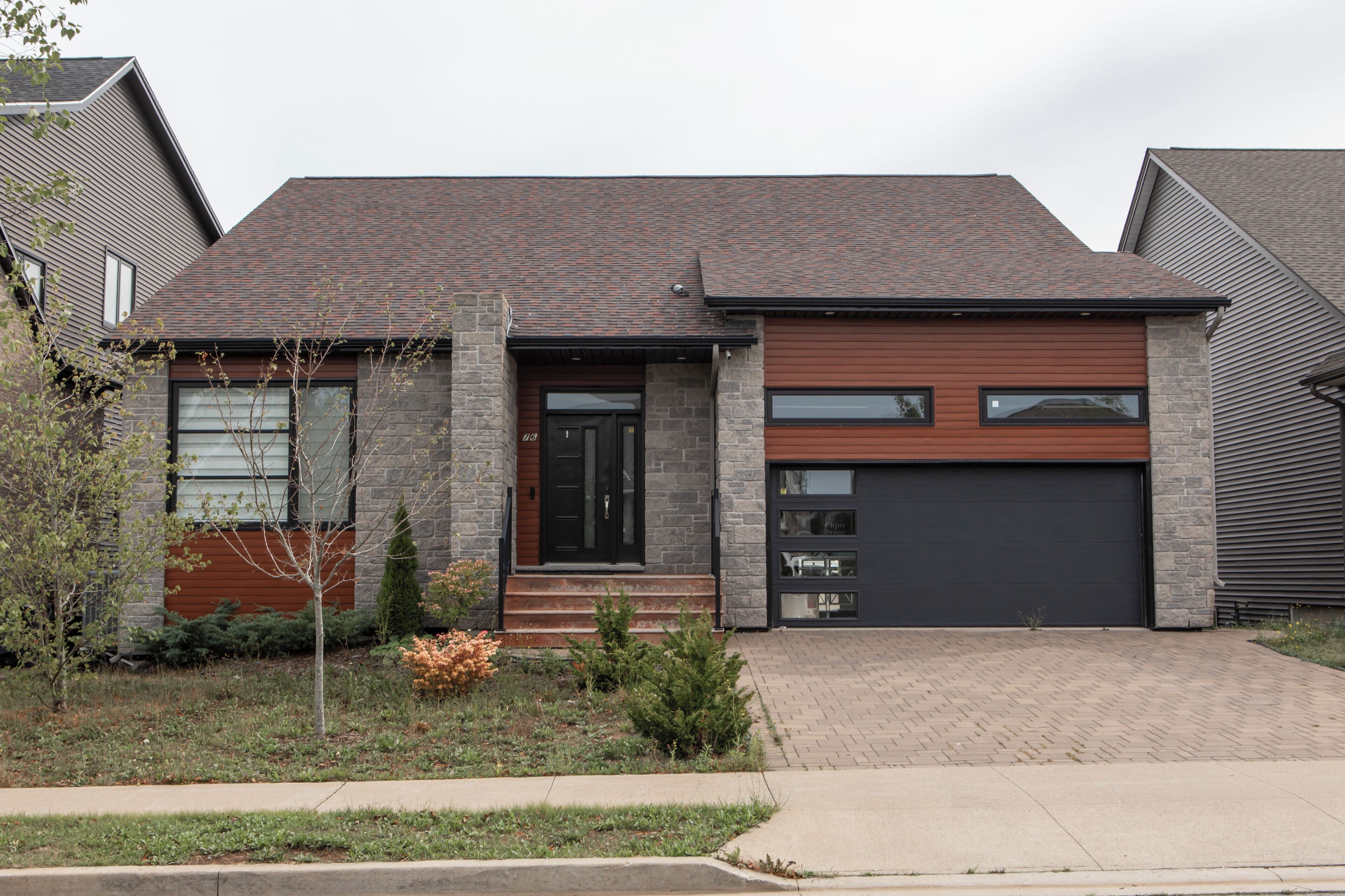 A modern two-story house with a brick exterior, a dark garage door, and a front porch with steps.