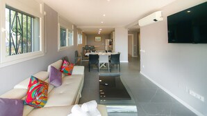 A modern living room with a sofa, a dining area, and a TV mounted on the wall. - WELCS APARTMENT 282 EMP in villa with swimming pool com (Rosas / Roses)
