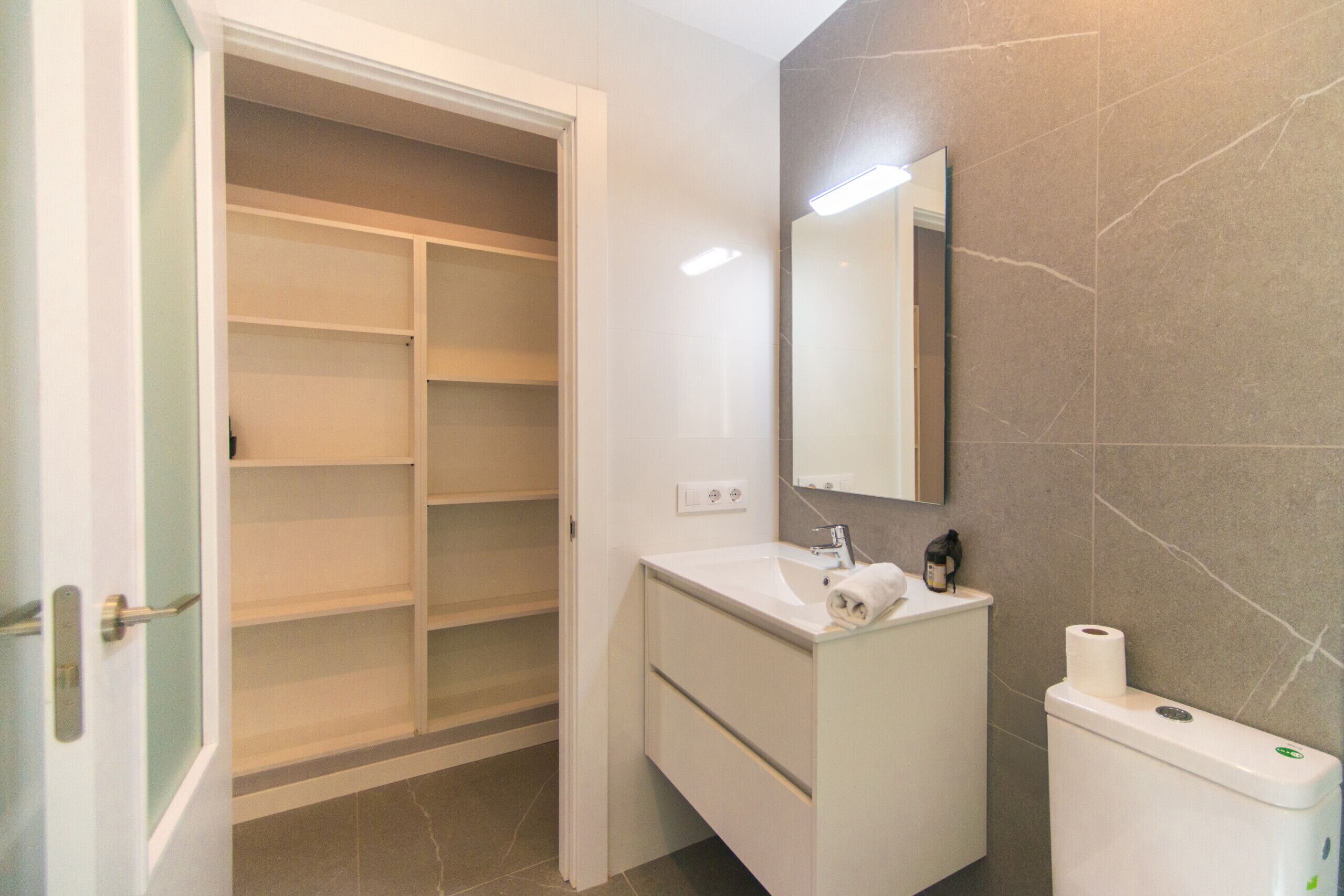 Une salle de bain avec un lavabo blanc, un miroir, des toilettes et un dressing.
