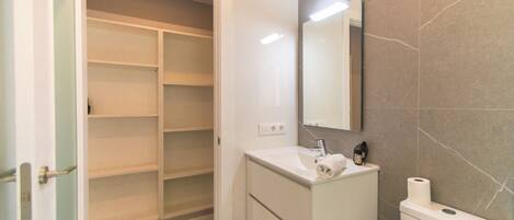 Une salle de bain avec un lavabo blanc, un miroir, des toilettes et un dressing.