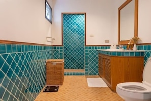 A bathroom with a tiled floor, a wooden vanity, a white toilet, and a shower area with a blue-tiled wall. - CoconutPalmsJacuzzipoolhugeproperty v136 (Rawai)
