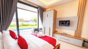 A bedroom with a large bed, a TV mounted on the wall, and a view of a swimming pool outside. - Gula Busa Guest House (Sukawati)