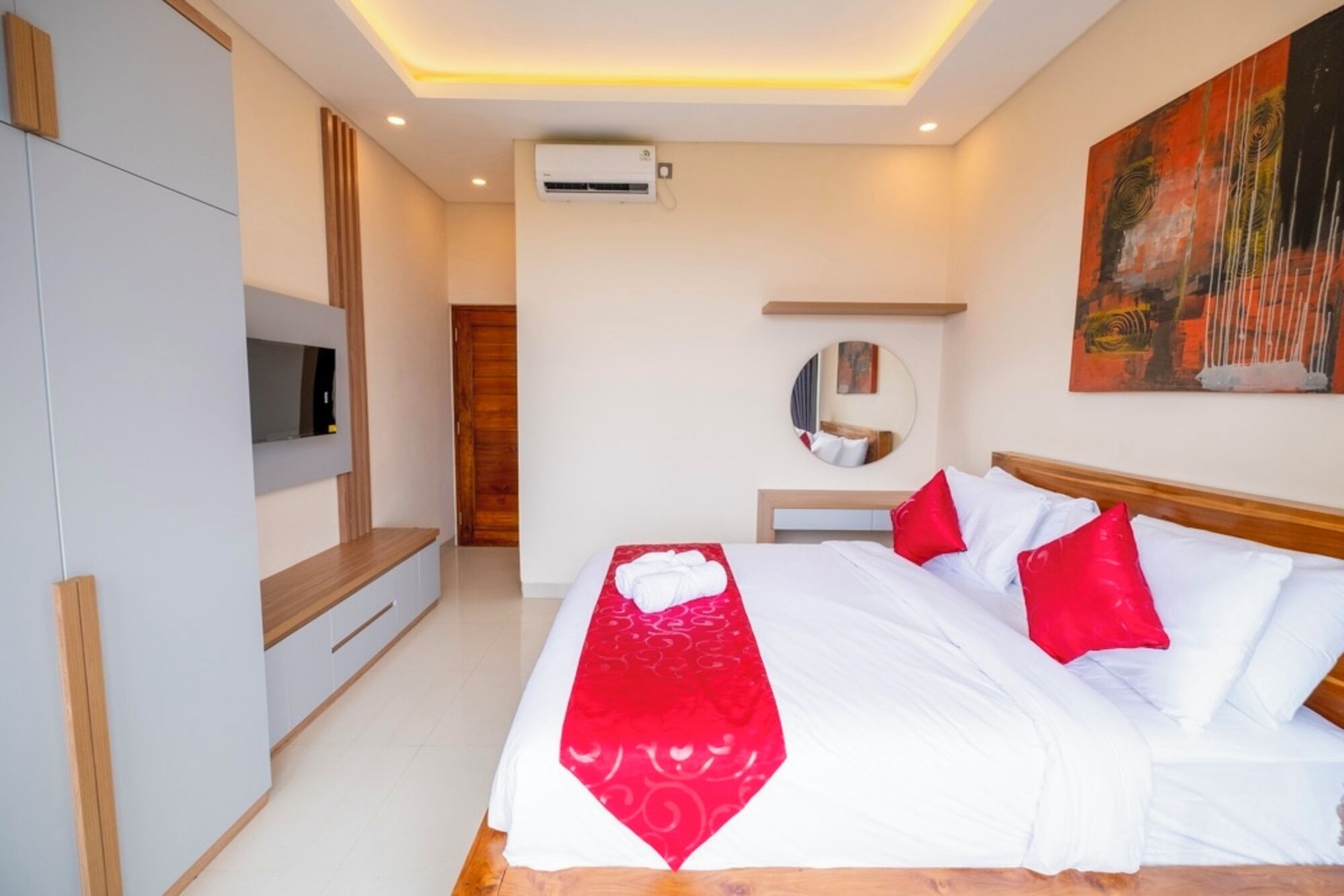 A modern hotel room with a bed, a TV, an air conditioning unit, and a painting on the wall.