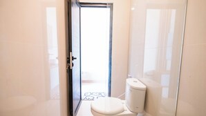 A modern bathroom with a toilet, a glass shower enclosure, and a tiled floor. - Gula Busa Guest House (Sukawati)