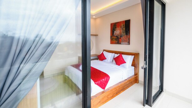 A modern bedroom with a large bed, a painting on the wall, and a glass door leading to a balcony. - Gula Busa Guest House (Sukawati)