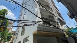 A multi-story residential building with a garage entrance, a parked motorcycle, and visible electrical wiring. - LUMI WEST LAKE APARTMENT (Hanoi)