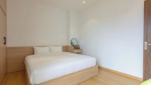 A modern bedroom with a large bed, wooden headboard, and a small bedside table with a plant. - LUMI WEST LAKE APARTMENT (Hanoi)