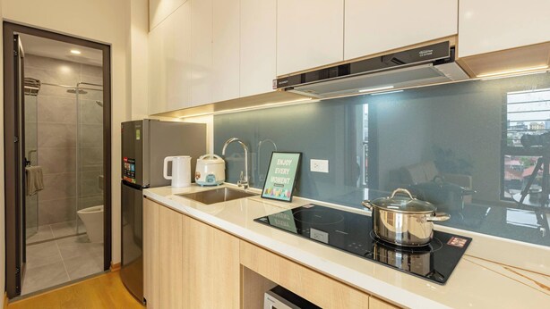 A modern kitchen with a built-in oven, a sink, and a glass shower enclosure. - LUMI WEST LAKE APARTMENT (Hanoi)