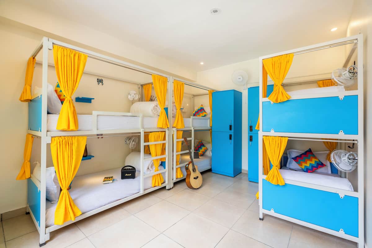 A room with bunk beds, each with yellow curtains, a guitar, and a fan.