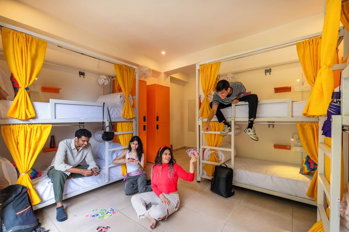 A dormitory room with bunk beds, a fan, and a suitcase on the floor.