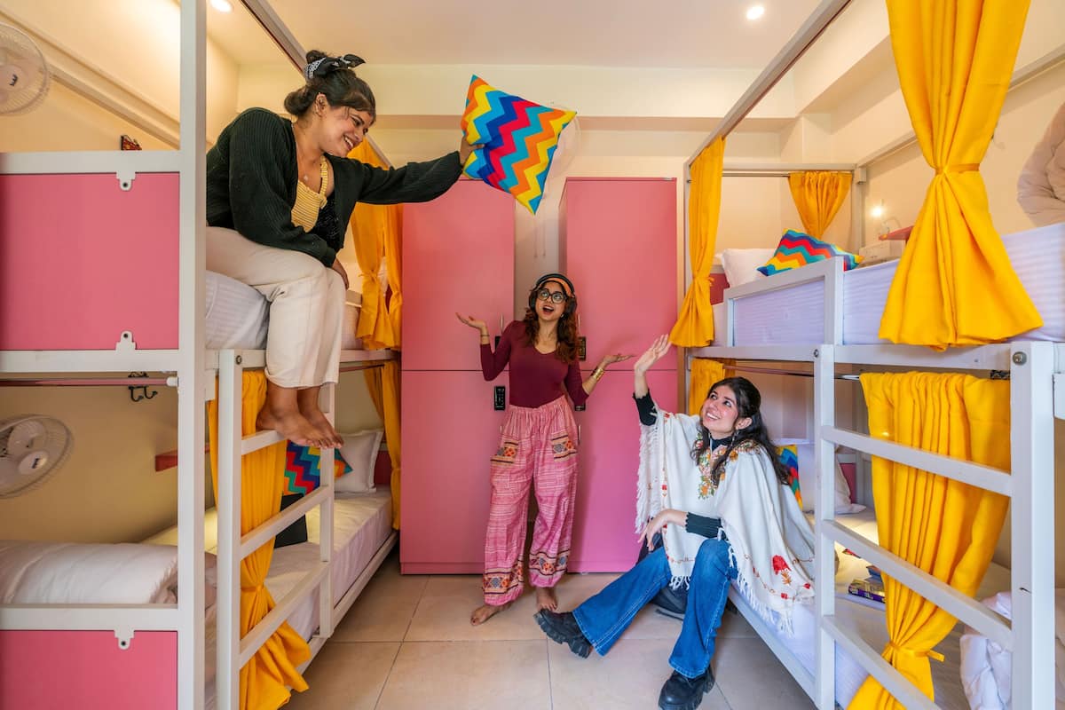A bunk bed room with pink and yellow curtains, a fan, and a colorful zigzag pillow.