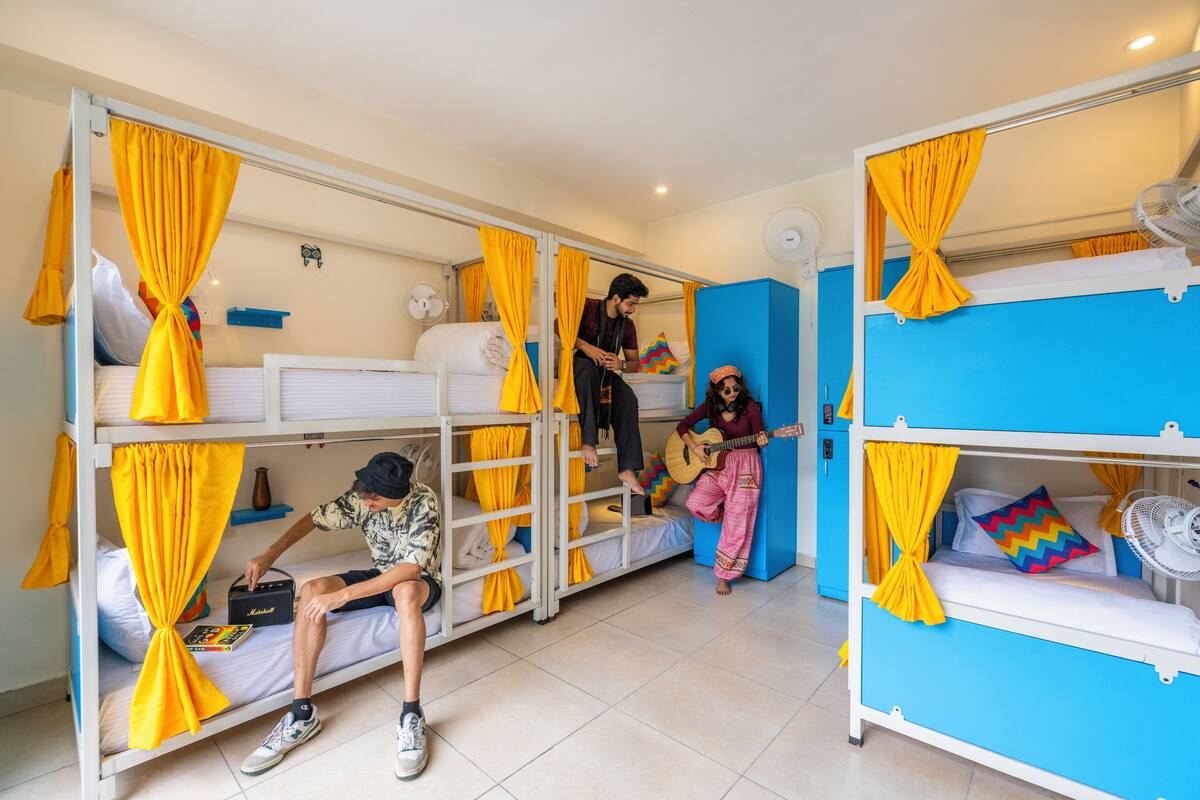 A dormitory room with bunk beds, yellow curtains, and a fan.