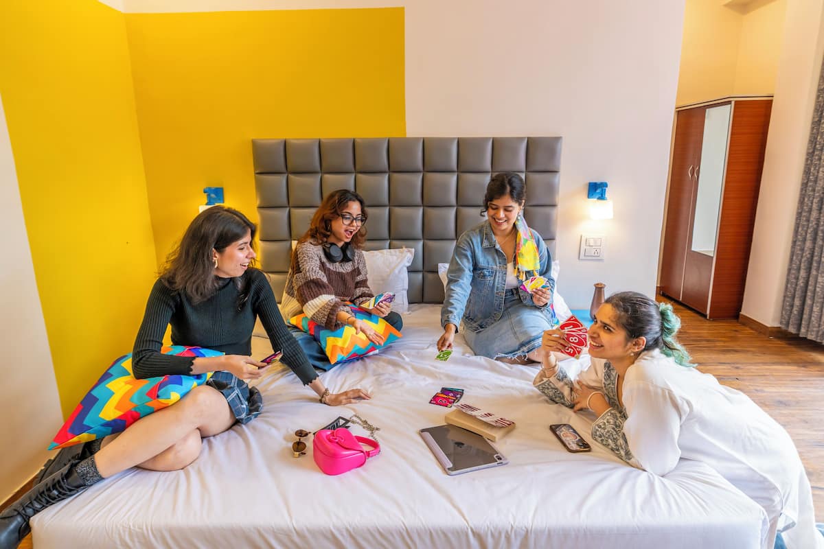 A group of people sitting on a bed in a room with a yellow wall and a grey headboard.