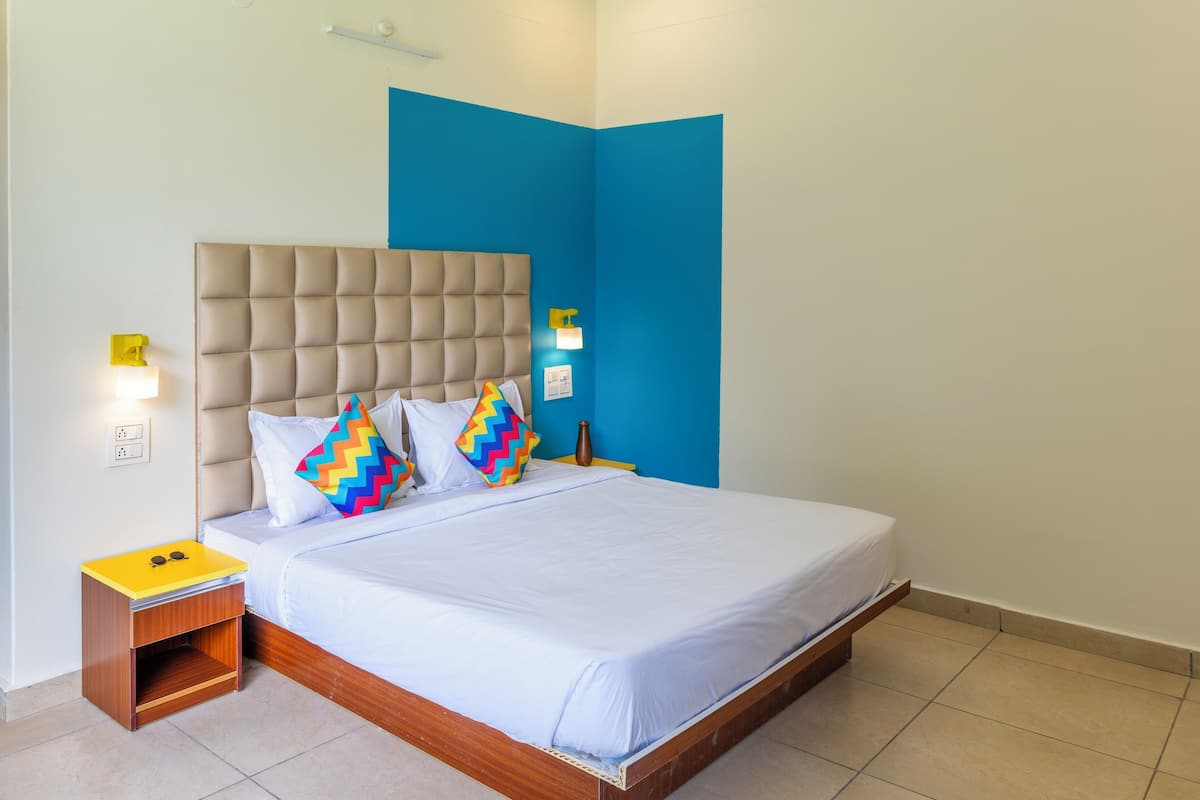 A neatly made bed with a tufted headboard, a bedside table with a lamp, and a wall-mounted light fixture.