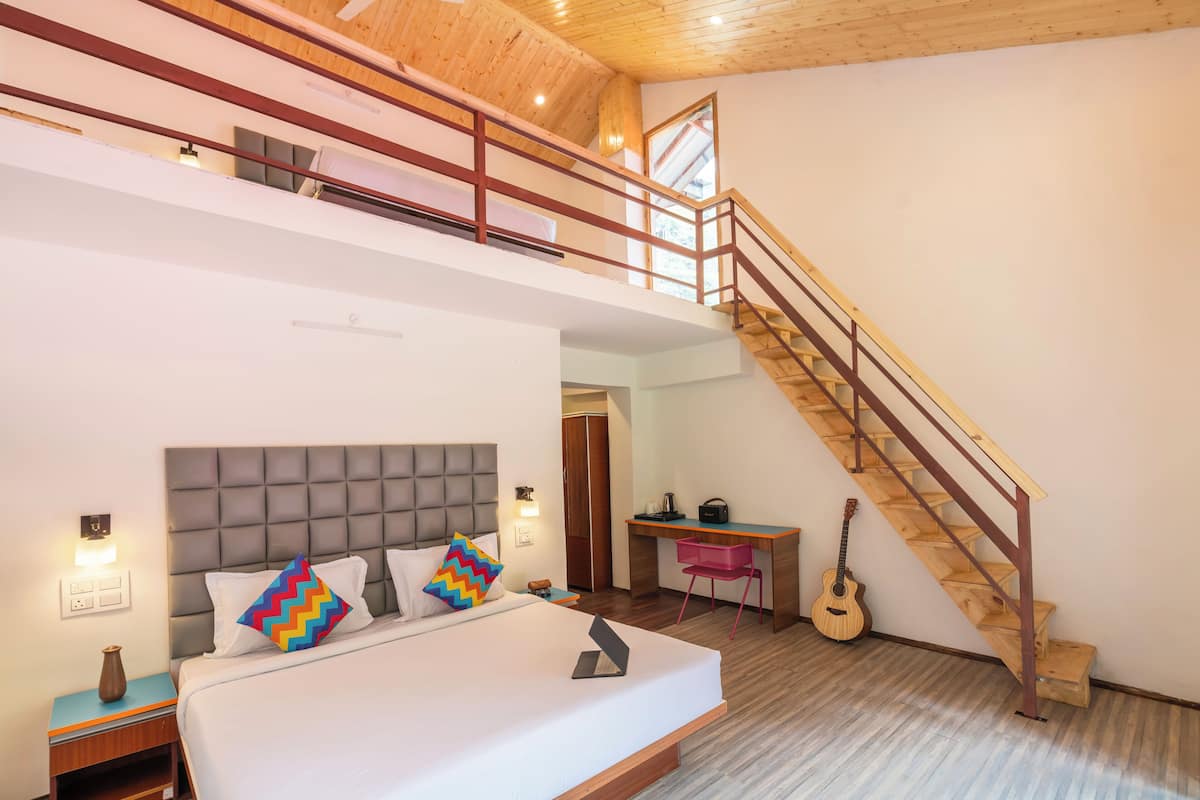 A bedroom with a bed, a desk, a guitar, and a staircase.