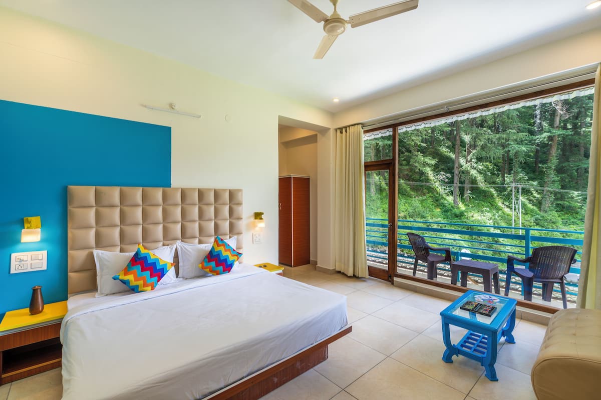 A hotel room with a large bed, a balcony with chairs, and a view of a forest.