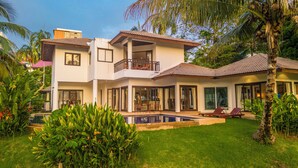 A two-story house with a swimming pool, surrounded by lush greenery and palm trees. - MassiveHugePool9MinutesWalk to BeachV131 (Choeng Thale)