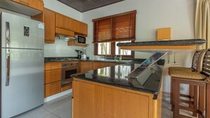 A kitchen with wooden cabinets, a stainless steel refrigerator, a microwave, and a granite countertop. - MassiveHugePool9MinutesWalk to BeachV131 (Choeng Thale)