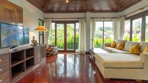 A spacious living room with a wooden floor, a large flat-screen TV, a sofa with cushions, and a cabinet with drawers. - MassiveHugePool9MinutesWalk to BeachV131 (Choeng Thale)