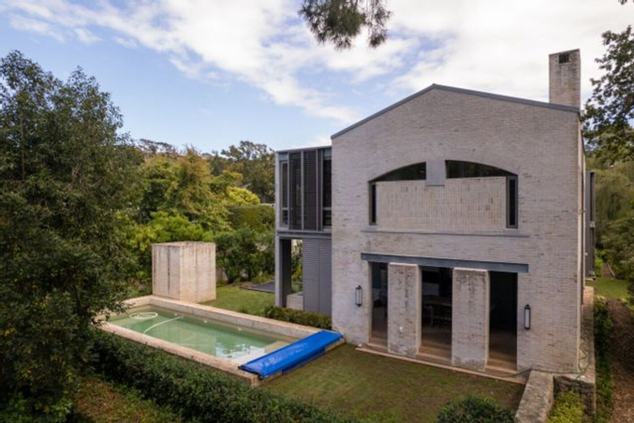 Ein modernes, zweistöckiges Haus mit Swimmingpool, umgeben von üppigem Grün.