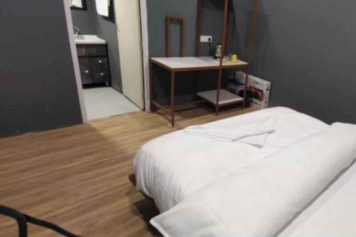 A bedroom with a bed, a wooden floor, a desk, and a mirror.