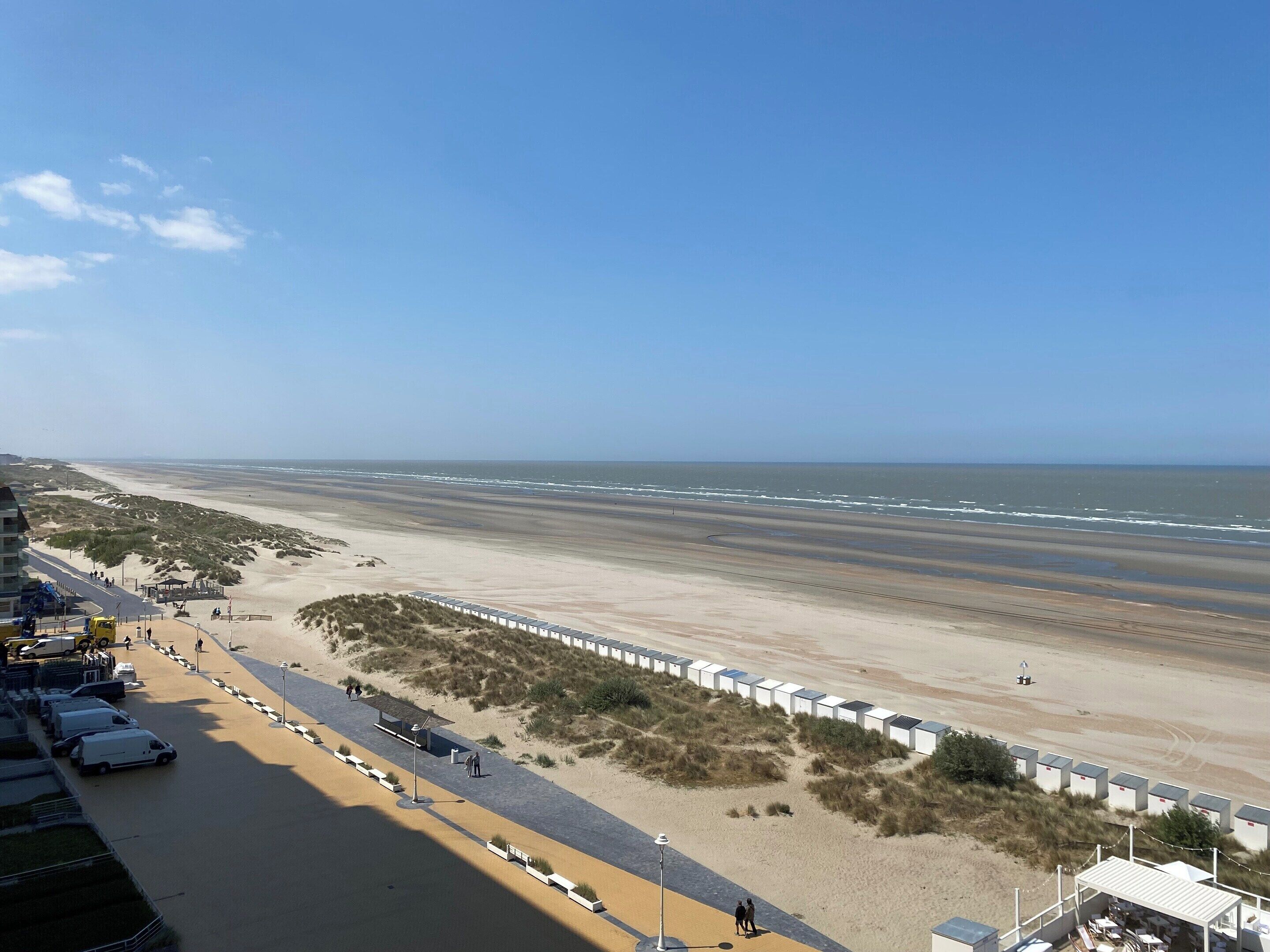 A beach with a row of beach huts, a parking area, and a road leading to the beach.