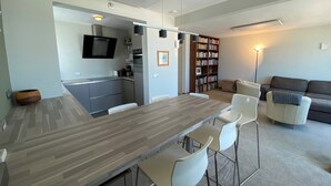 A modern kitchen with a central island, a dining area with bar stools, a living room with a sofa, and a bookshelf. - Apartment in Nieuwpoort-bad With Sea View (Nieuwpoort)
