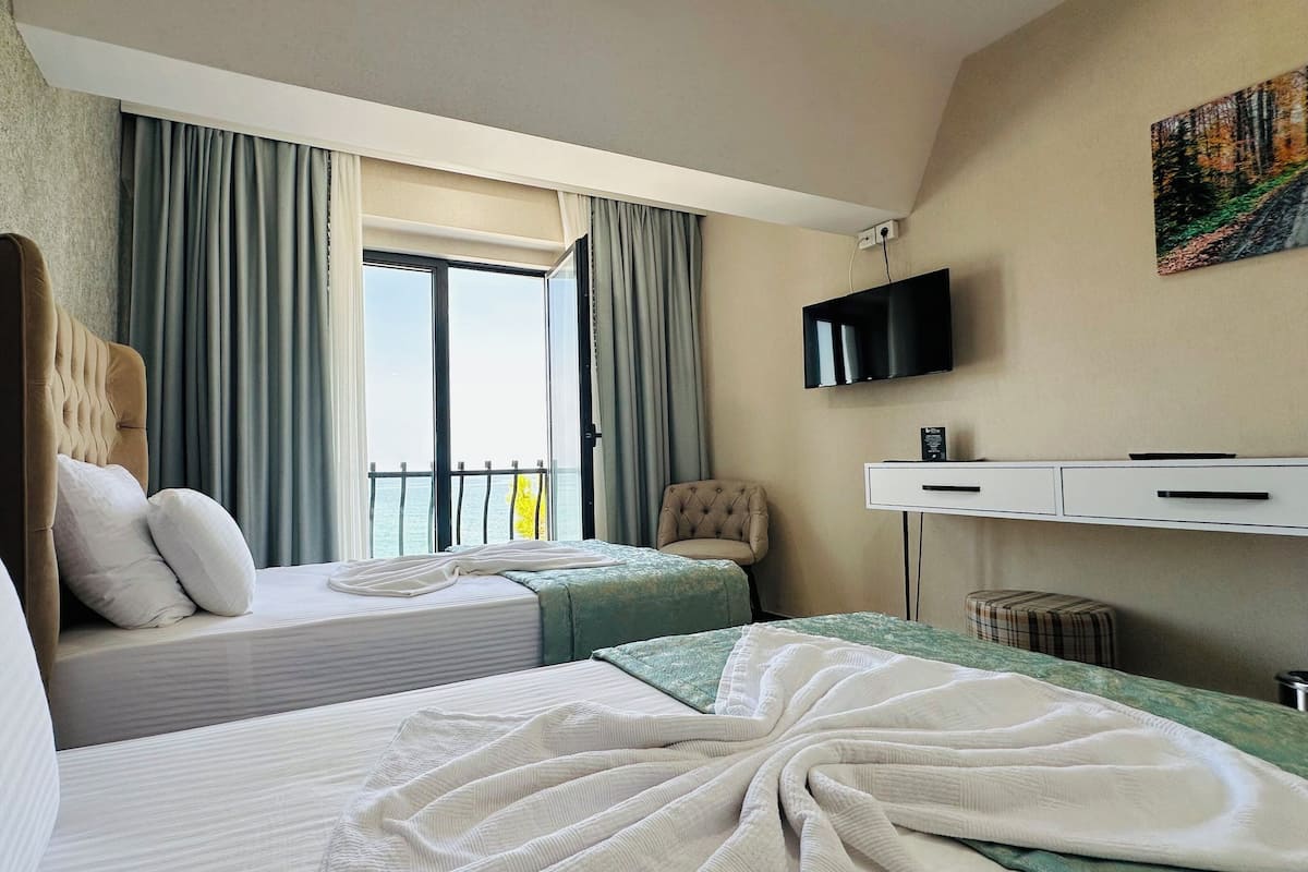 A hotel room with two beds, a television, a desk, and a view of the sea.