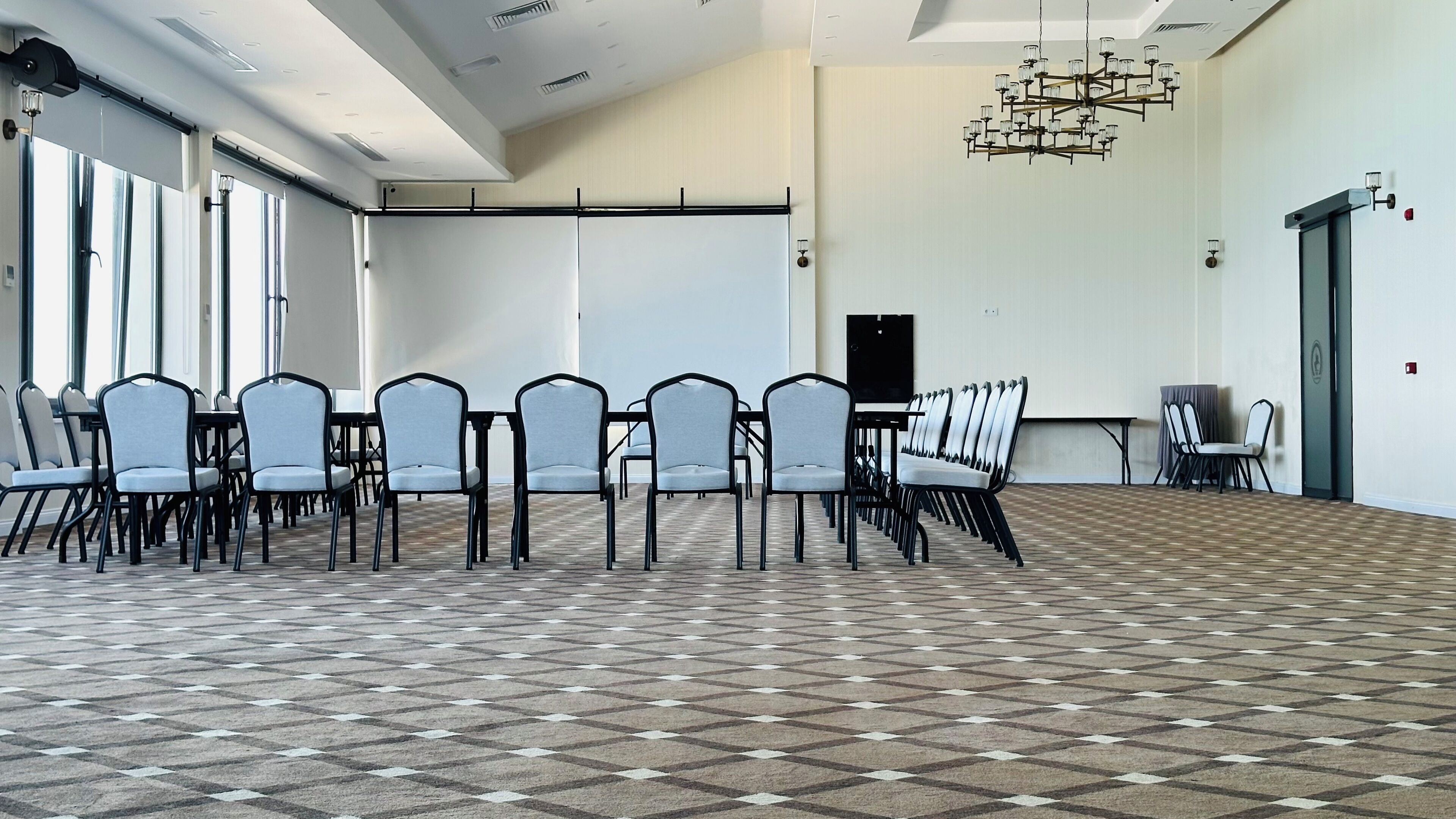 A conference room with a checkered floor, rows of chairs, a projector screen, and a chandelier.