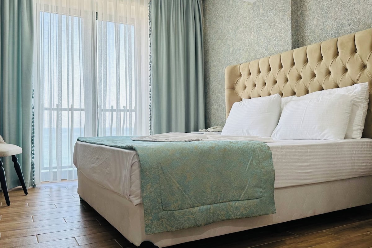 A bedroom with a tufted headboard, a bed with white linens, a green throw blanket, and a chair with a light-colored cushion.